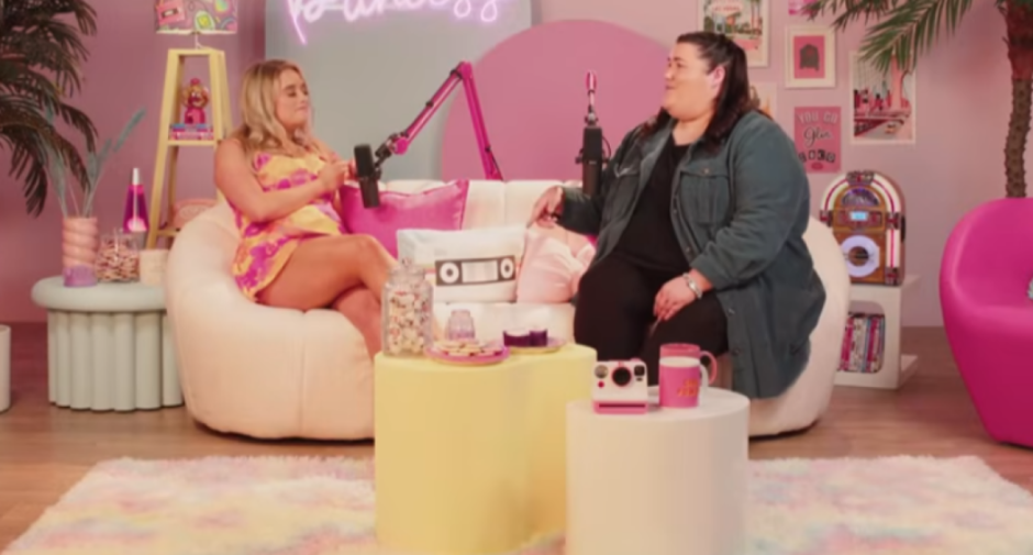 Two women in a pink studio recording a podcast.