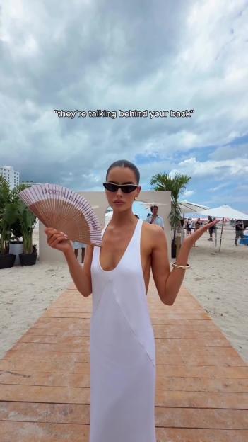 Maura Higgins in a white dress, holding a fan, at the Sports Illustrated Swimsuit Beach Club.