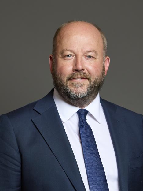 Portrait of a man with a beard and bald head wearing a navy suit and tie.