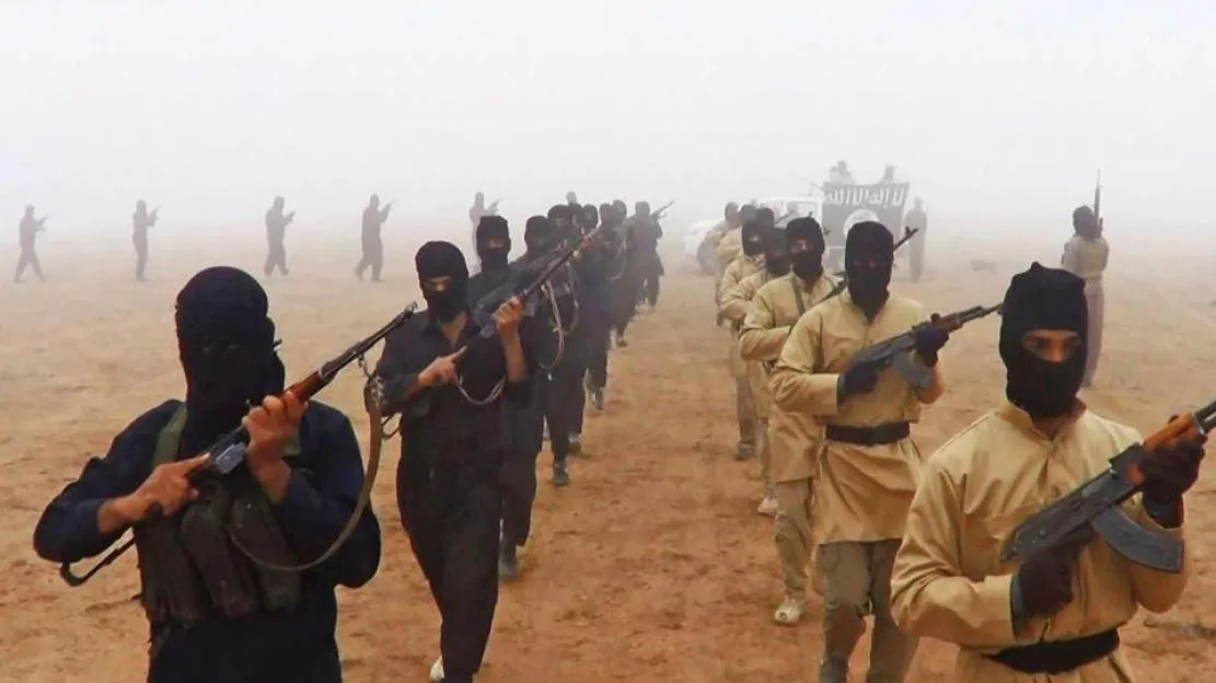 Islamic State of Iraq and the Levant fighters march in a line through a dusty area, carrying rifles and wearing face coverings.