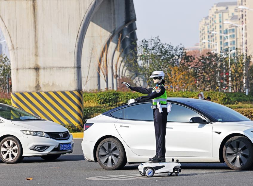 A humanoid robot in a traffic police uniform directs traffic on a street.