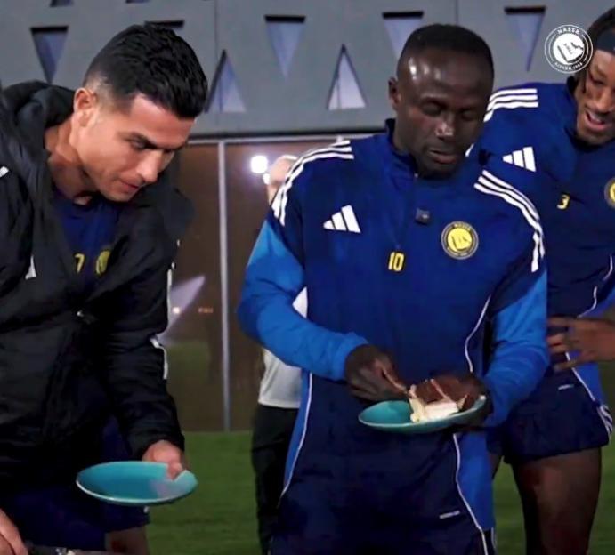 Football players Ronaldo and Mané eating cake from plates.