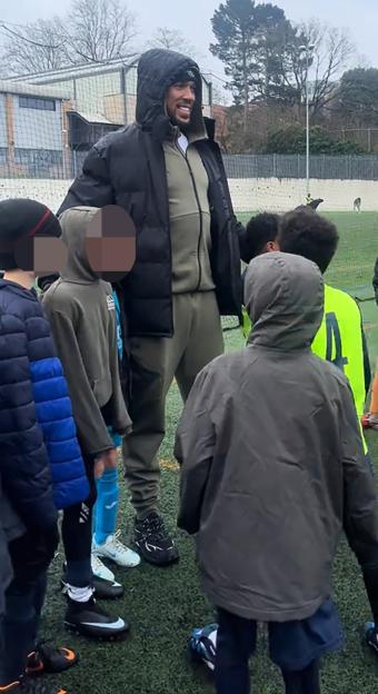 Anthony Joshua smiling while standing with children on a football pitch.