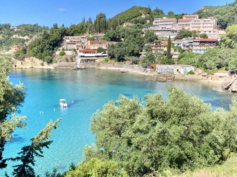 Agia Triada beach, Paleokastritsa, Corfu, Greece, with a clear turquoise bay and houses nestled on the green hills.