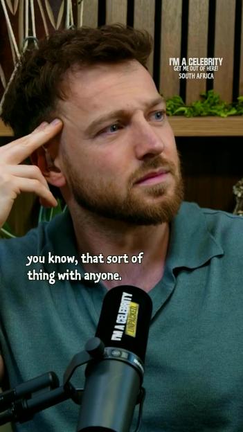 A man with short brown hair and a beard, wearing a teal polo shirt, looks to the right while resting his hand on his temple. A microphone with the text "I'M A CELEBRITY UNPACKED" is visible in the foreground, and text in the upper right says "I'M A CELEBRITY GET ME OUT OF HERE! SOUTH AFRICA". The caption "you know, that sort of thing with anyone." is overlaid on the lower left of the image.