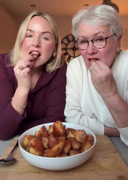 Two women eating roasted potatoes from a white bowl.