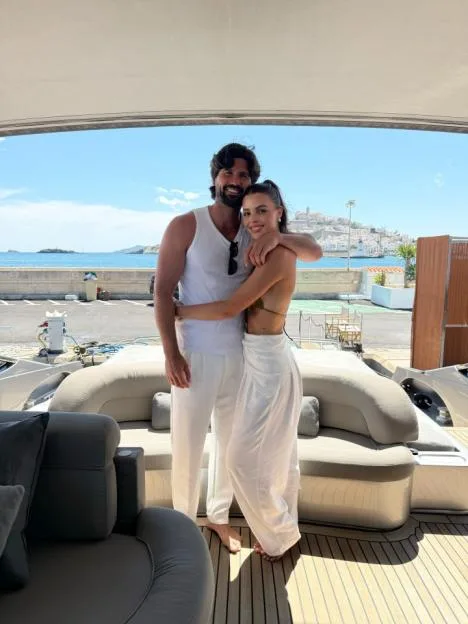 A smiling couple embracing each other on a yacht with a coastal town in the background.