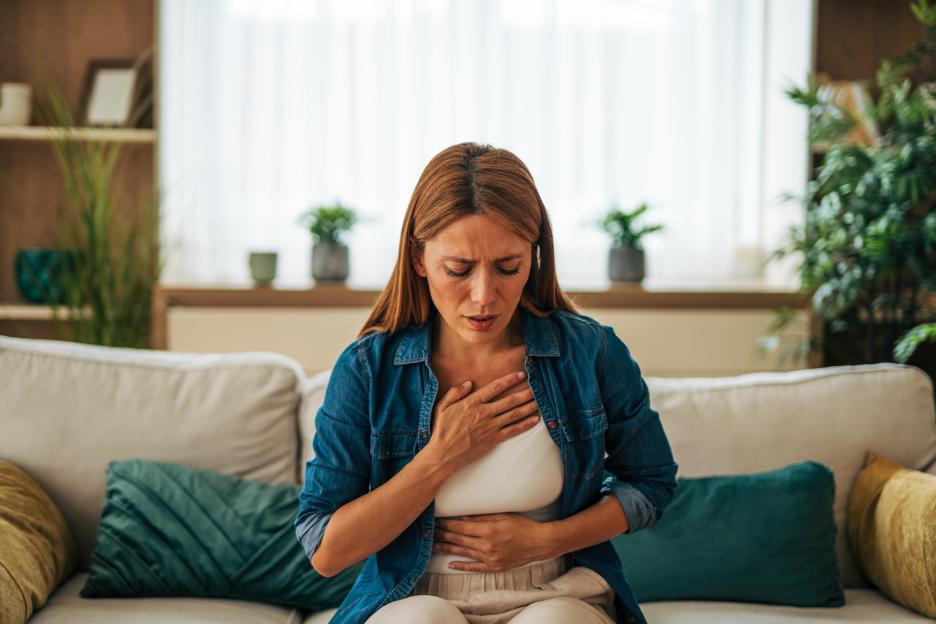Woman sitting on a sofa, clutching her chest and stomach in pain.