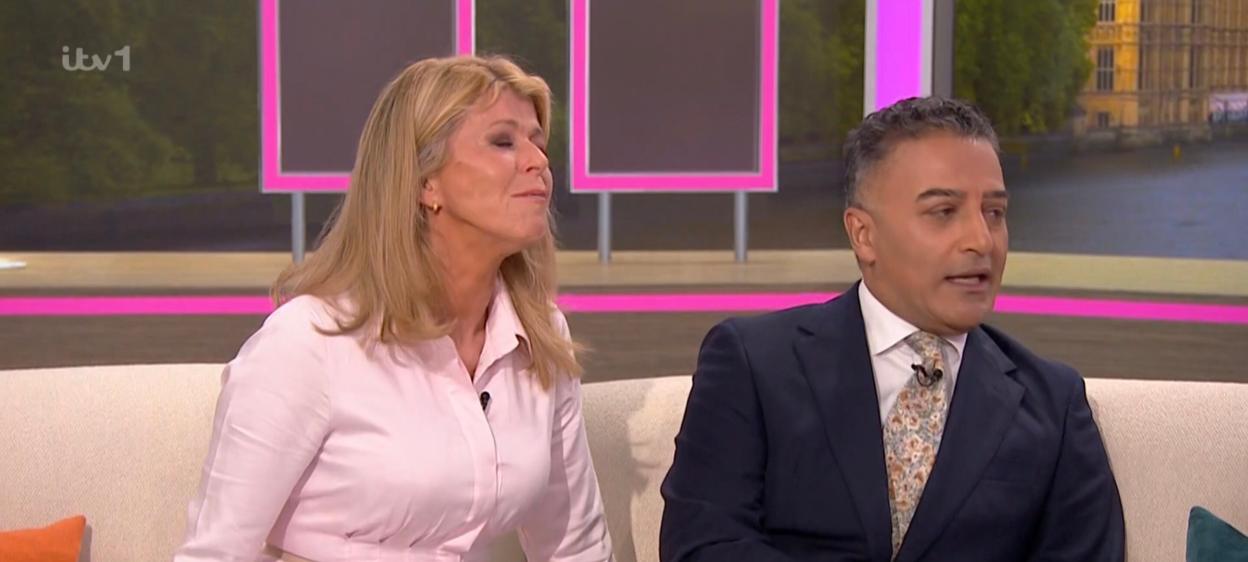 Kate Garraway and a male co-host on a TV show, with "AMY & CARLOS STARS SPENT 2 WEEKS ON THE RUN" on a ticker below.