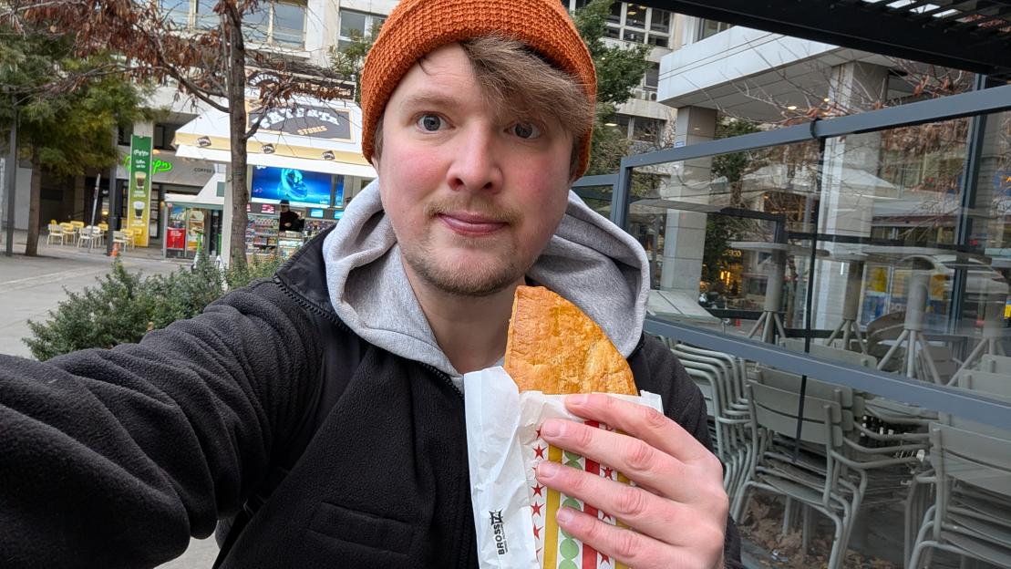 A man wearing an orange hat holding a pastry in front of Gregory's bakery.