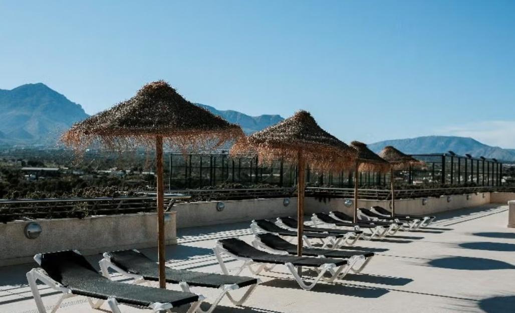 Rooftop terrace with straw umbrellas and lounge chairs overlooking mountains.