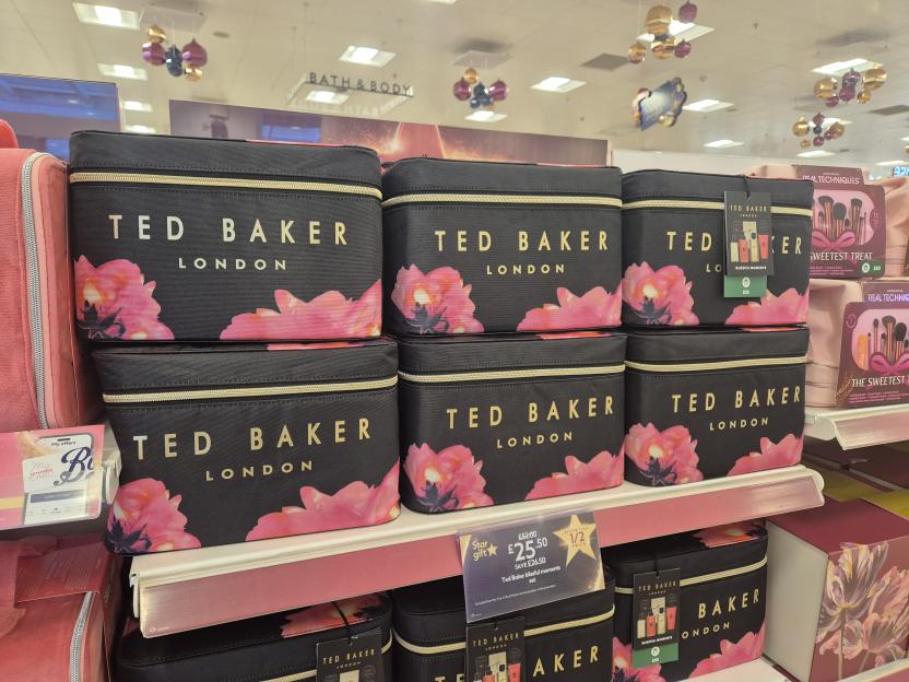Multiple Ted Baker London "Blissful Moments" gift sets with black makeup bags featuring pink floral designs on a store shelf.
