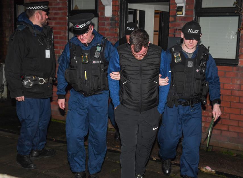 Police escorting an arrested man out of a house during a drug raid.