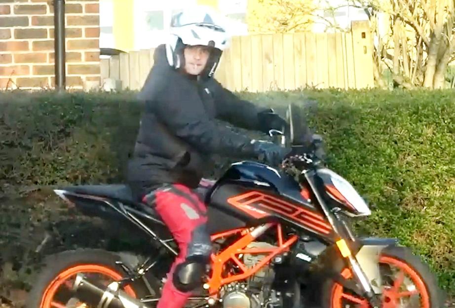 A man in a helmet and black jacket on a motorbike, with red pants and knee pads.