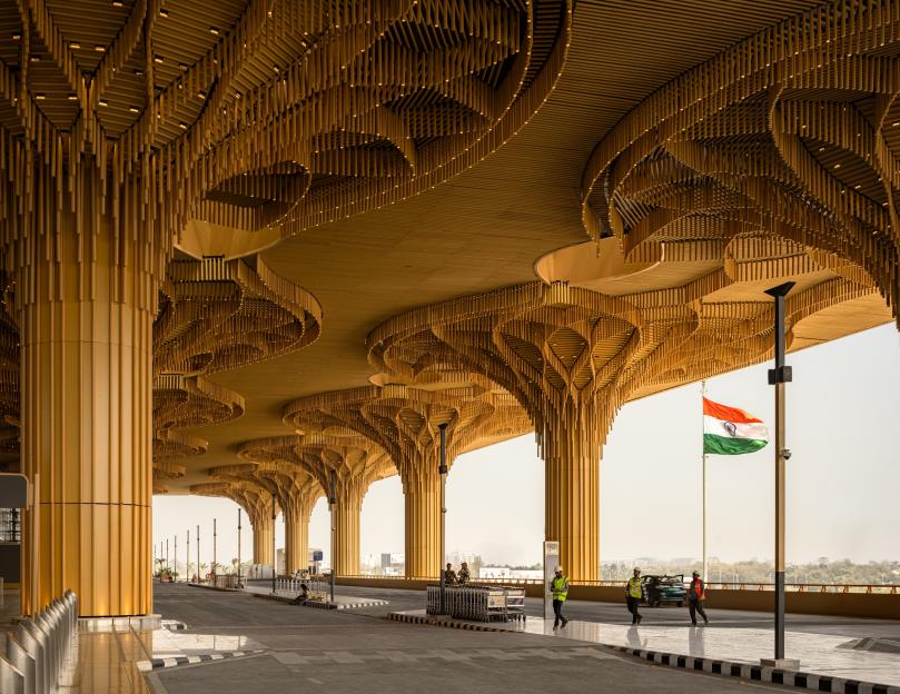 Exterior of an airport terminal with golden, tree-like columns and a large Indian flag.