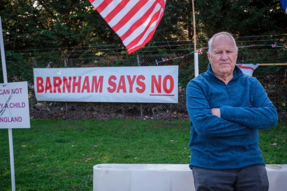 Protestor Les Day stands in front of a "Barnham Says No" banner at MOD Barnham.