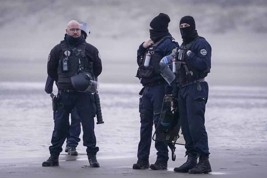 Three police officers in tactical gear standing on a wet surface.