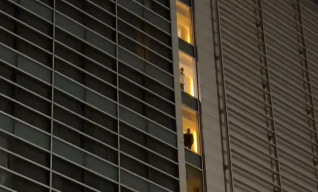 Two people standing in illuminated windows of a tall building at night.