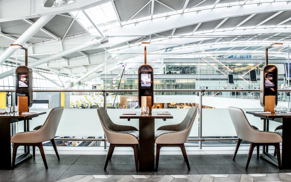 Tables and chairs with a digital menu in Gordon Ramsay's Plane Food Market at Heathrow Airport.