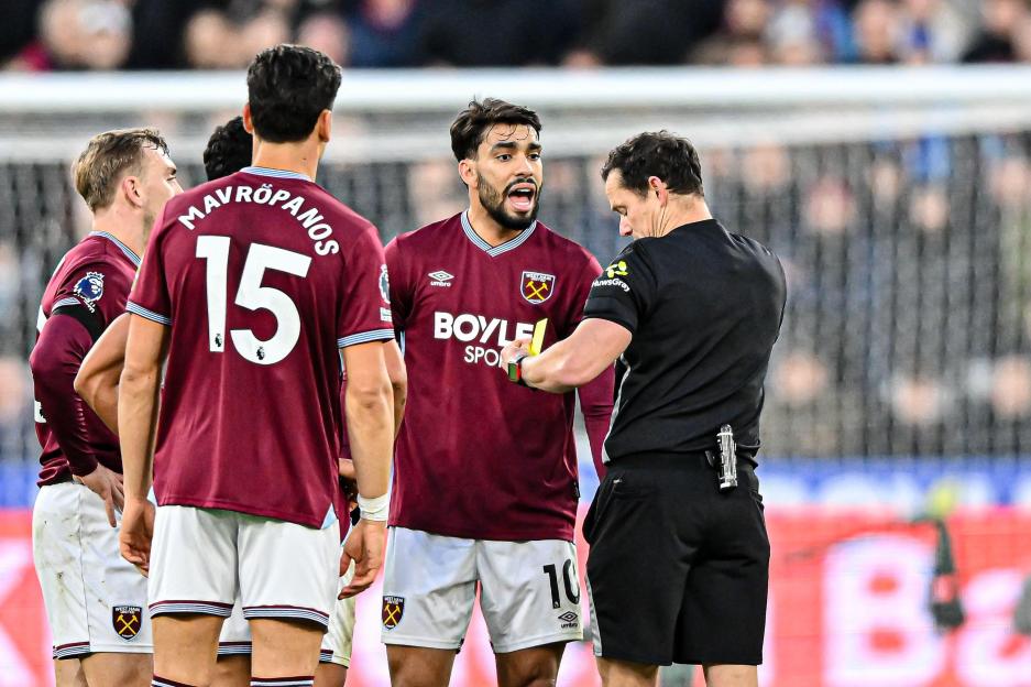 Lucas Paqueta argues with referee Darren England as the referee holds up a yellow card during a soccer match.