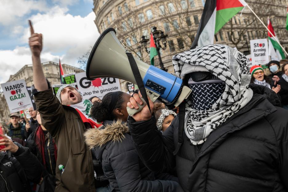Pro-Palestinian demonstrators protesting military actions in Gaza, with a person in a keffiyeh holding a megaphone.
