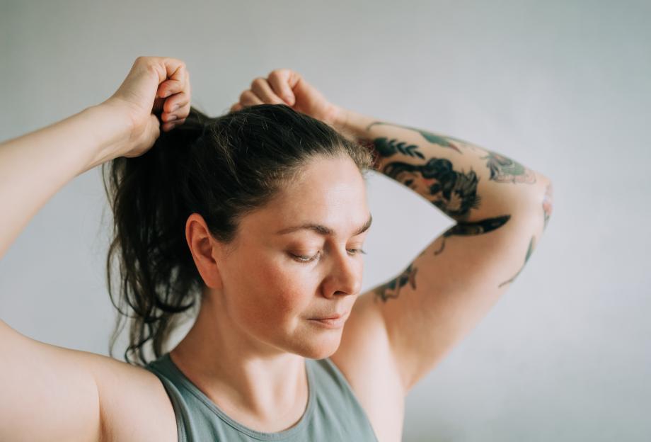 Woman with a tattooed arm tying her hair into a ponytail.