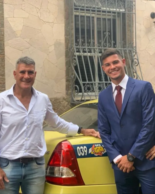 Two men posing in front of a yellow taxi.