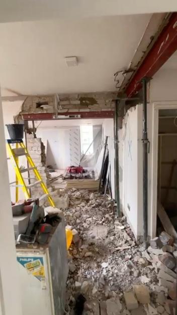 A room under construction with exposed brickwork, supporting beams, debris on the floor, and a ladder, reflecting a "cowboy builder" ruined dream home.