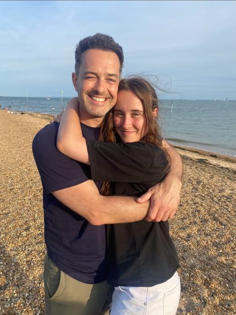 A man and a woman hugging on a beach, smiling at the camera.
