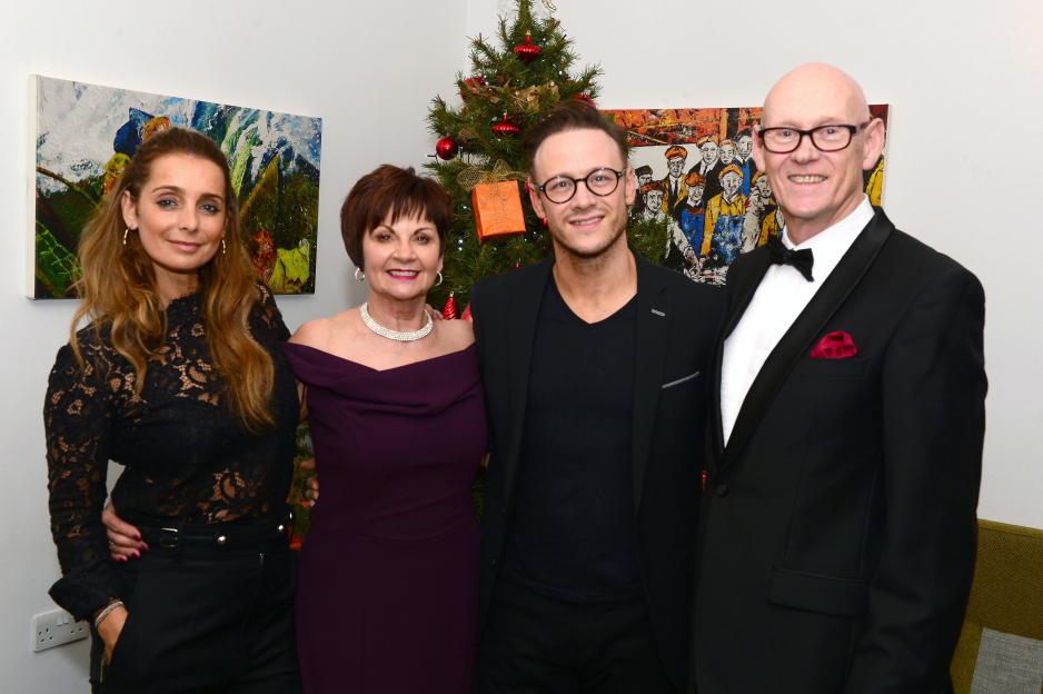 Four people pose for a photo in front of a Christmas tree.