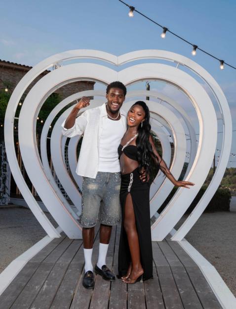 A man and a woman posing in front of a white heart-shaped tunnel.