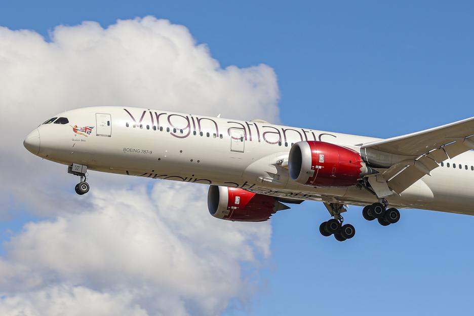 Virgin Atlantic Boeing 787 Dreamliner airplane landing with visible landing gear and engines against a partly cloudy blue sky.