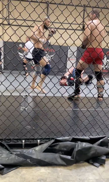 Mixed martial arts fighters sparring inside a cage, with one fighter on the ground.
