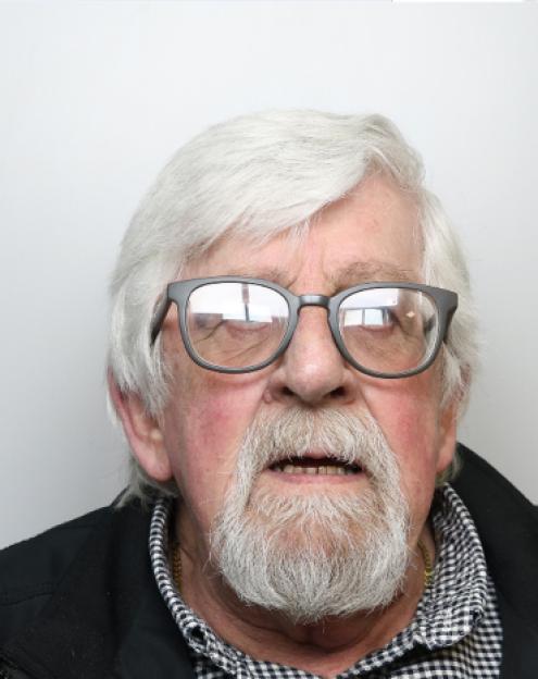 Mugshot of a white man with white hair, beard, and glasses.