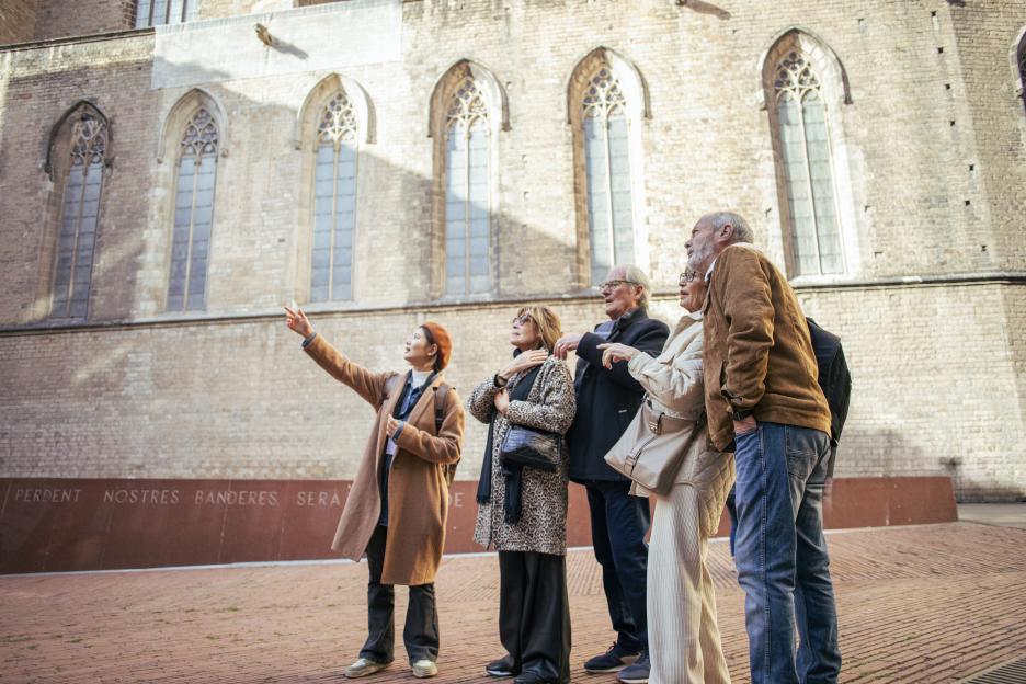 A tour guide pointing to a historic building for a group of senior tourists in Barcelona, Spain.