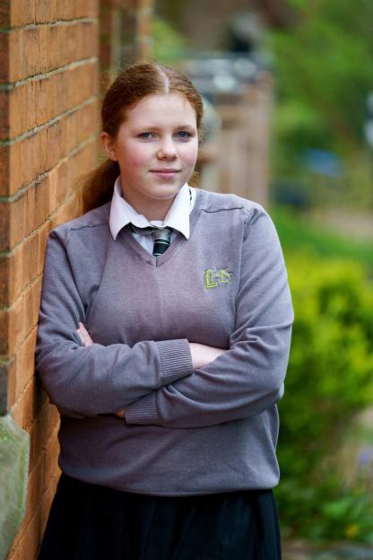 Phoebe Simmons, 12, in her banned school jumper, standing next to a brick wall.