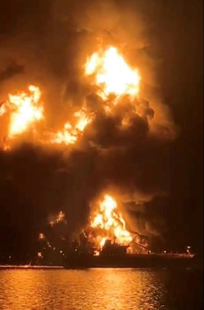 A ship is illuminated by fire from a burning vessel, after Iranian explosive-laden boats appear to have attacked two fuel tankers in Iraqi waters setting them ablaze
