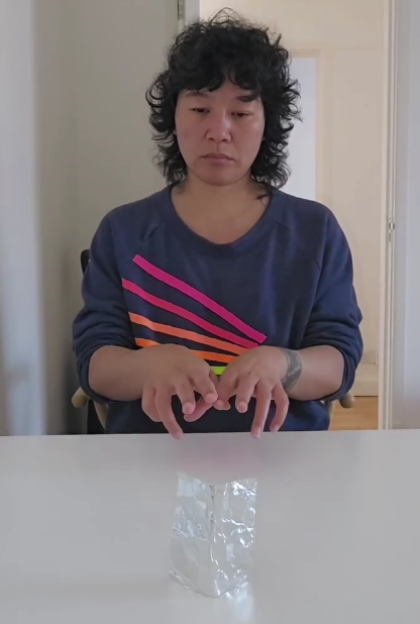 Garz Chan demonstrating telekinesis by hovering hands over a crinkled foil object on a white table.