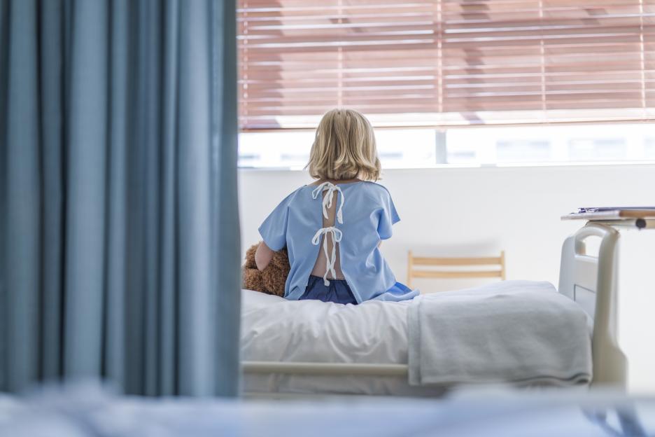 Rear view of a sick girl sitting on a hospital bed.
