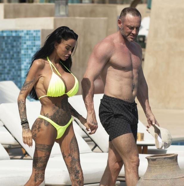 Newly married couple Katie Price and Lee Andrews holding hands while walking by a pool.