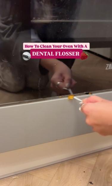 A person uses a dental flosser to clean the grime from around the edge of an oven door.
