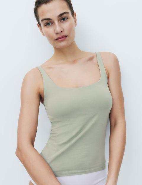 A woman with her hair pulled back models a light green scoop neck bra vest.