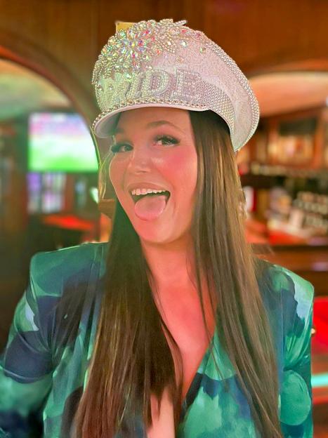 Samantha Murphy wearing a sparkling white hat and a green and black patterned top, sticking her tongue out.