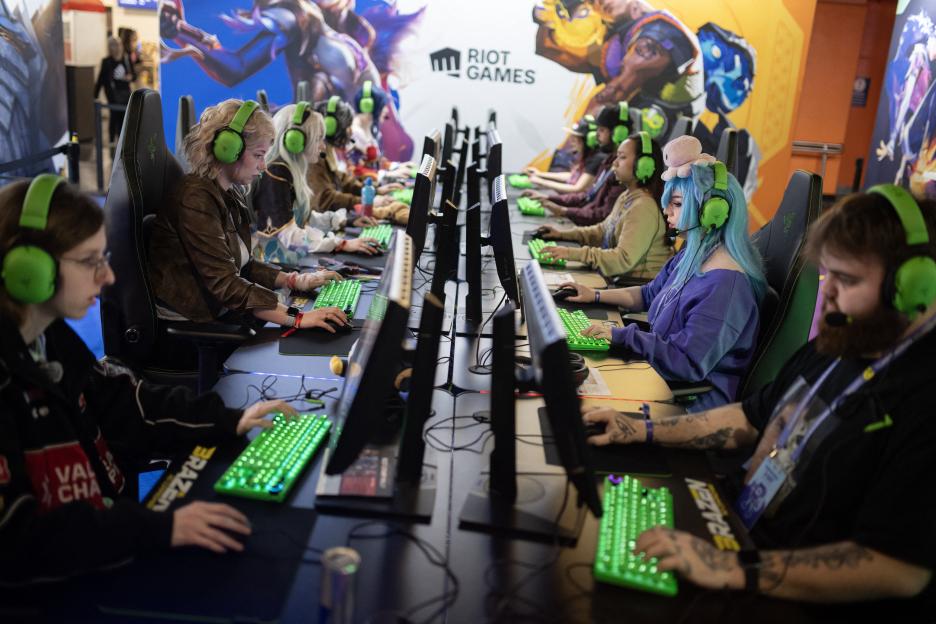 Multiple gamers with bright green headphones playing League of Legends at computers lined up at DreamHack.