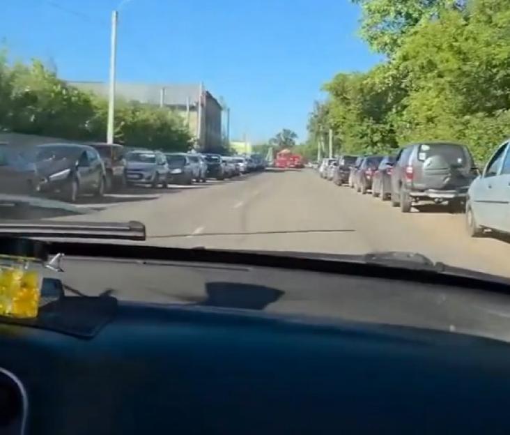 View from inside a car of a road with cars parked on both sides.