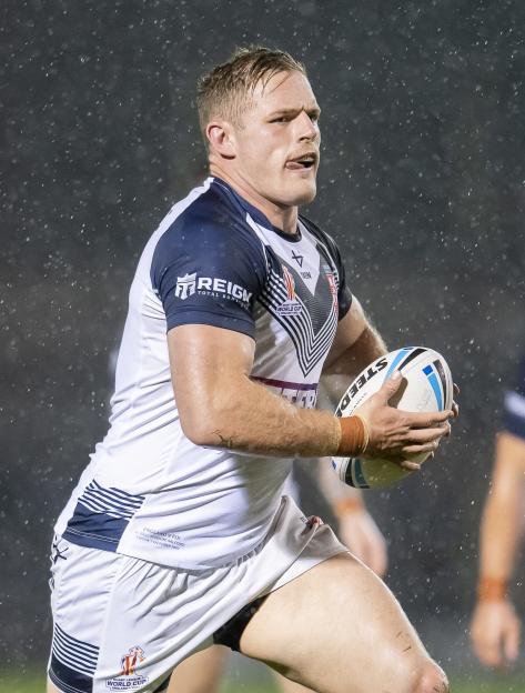 A rugby player from England wearing a white and blue jersey, holding a white rugby ball, and running in the rain.
