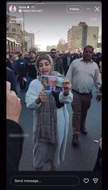 A woman in a crowd burns a photo of an older man in a suit while holding a lighter to it.