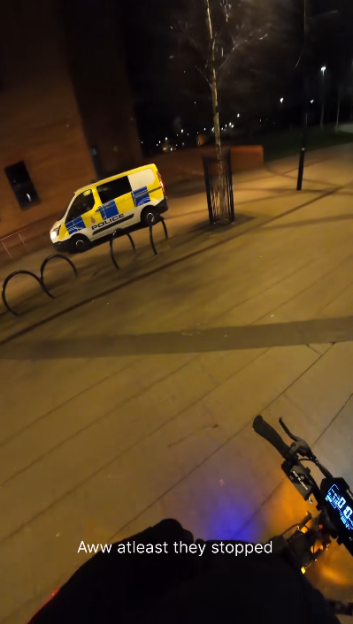 POV shot from an e-scooter of a police van parked behind bicycle racks at night.