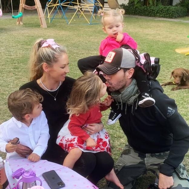 Anna Kournikova and Enrique Iglesias with their three children and a dog in a grassy yard.