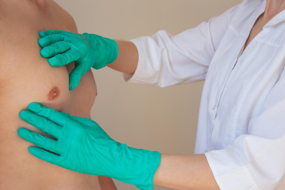 a doctor in green gloves examines a man's chest. Prevention of breast diseases in men.